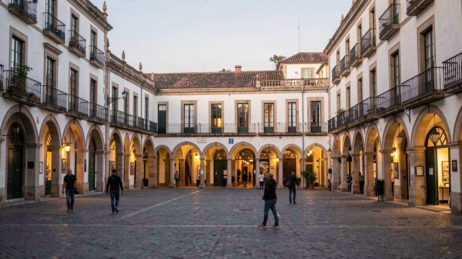 Vue de la Plaza Mayor de Valladolid au coucher du soleil, arcades éclairées, passants flous en premier plan, cadrage large au niveau du sol